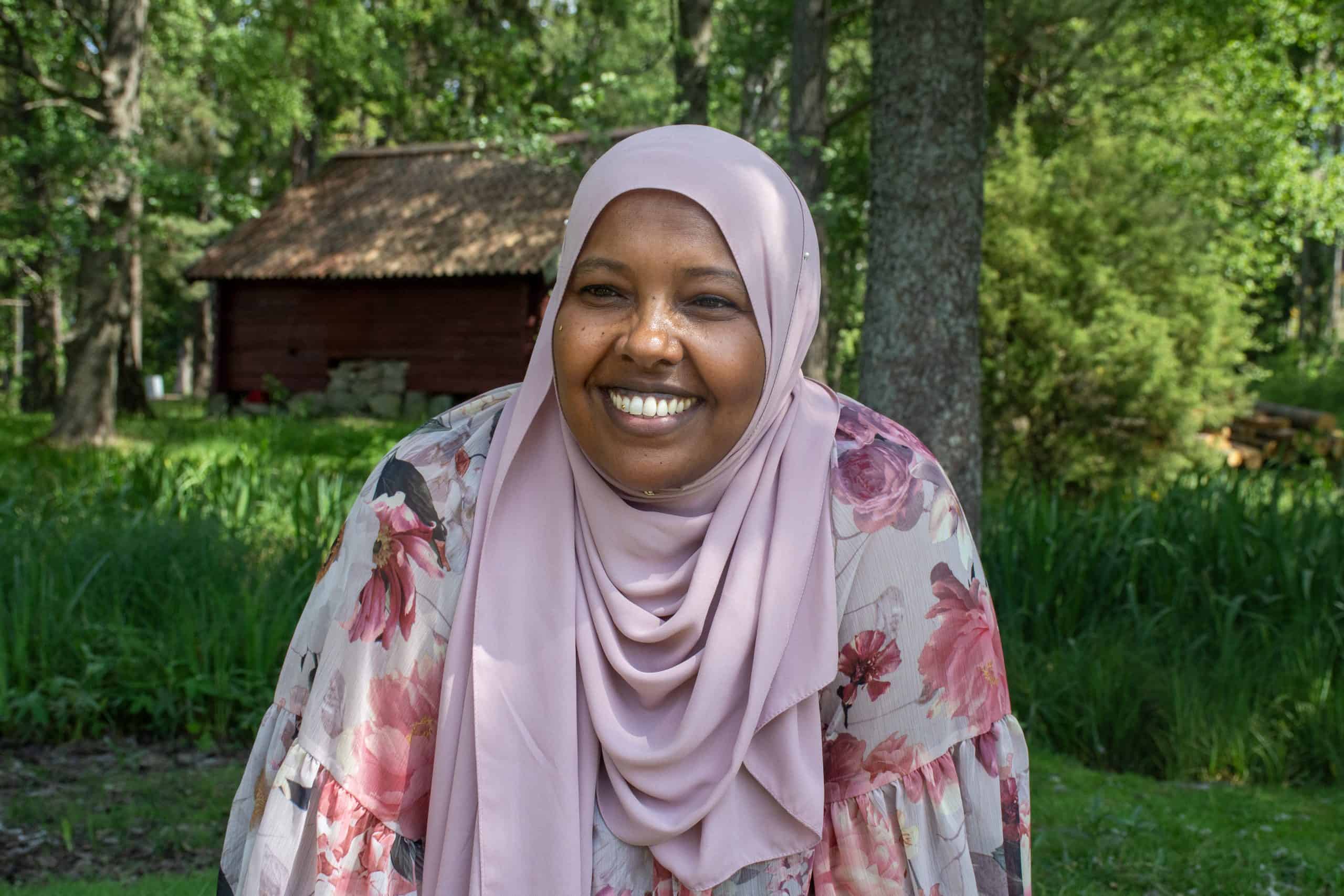 Glad kvinna i hijab utomhus i grönskande miljö.