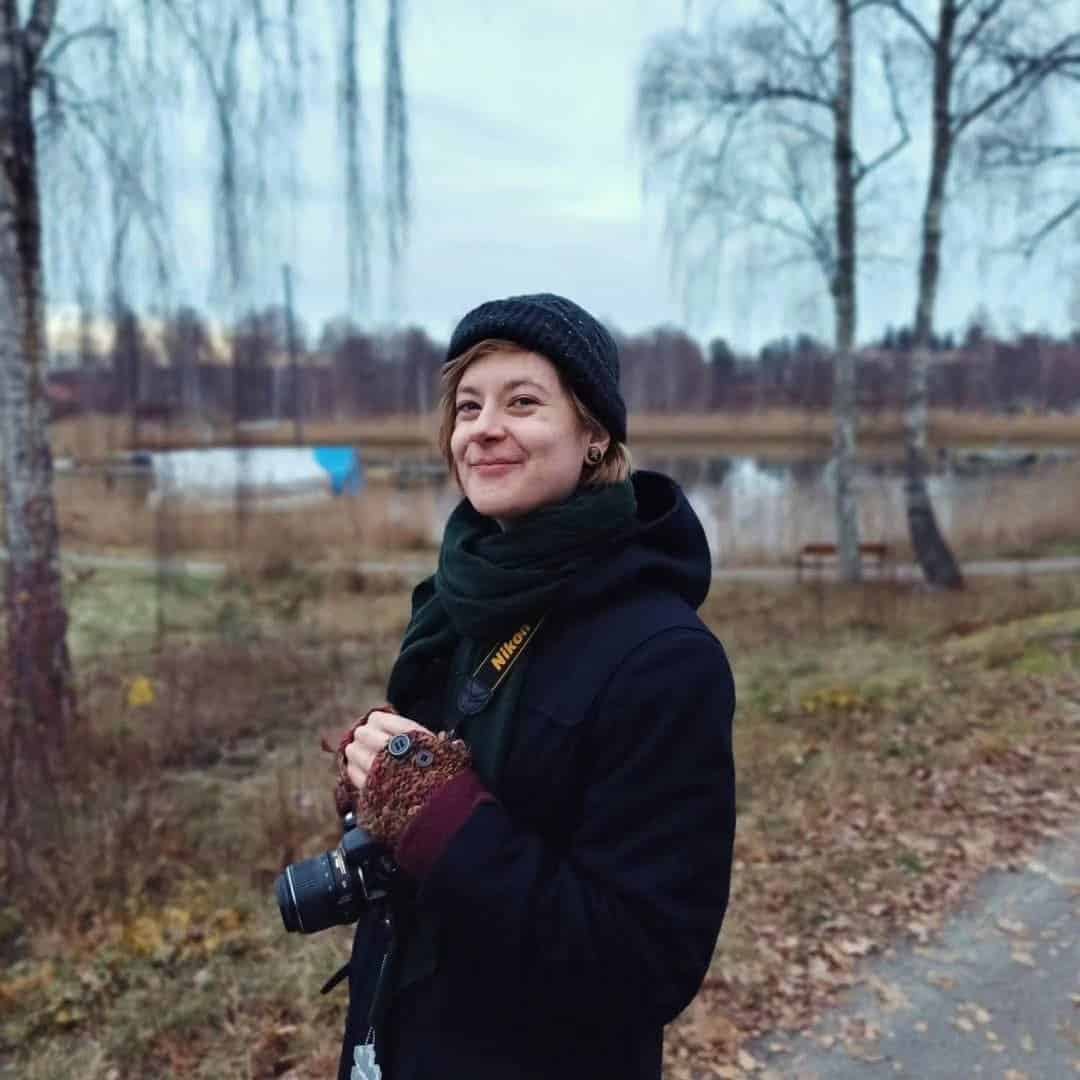 Ung kvinna med kamera vid sjö i höstlandskap, östra Södertörn.