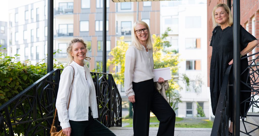 Tre blonda leende kvinnor som står utomhus.